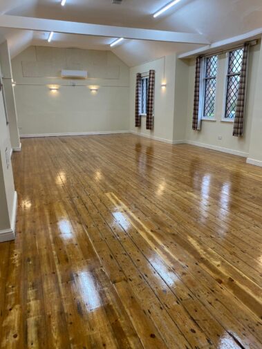 Empty community hall with a polished wooden floor and diamond-paned windows.