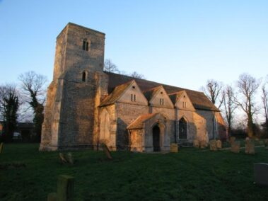 A stone church with a tall tower and several gables surrounded by a graveyard.