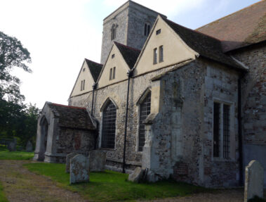 Stone church with multiple gables and a square tower, surrounded by a grassy churchyard.