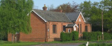 A single-storey red brick building with a slate roof and green hedges.