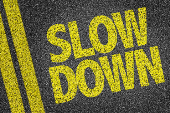 SLOW DOWN painted in yellow on a tarmac road with a double yellow line.