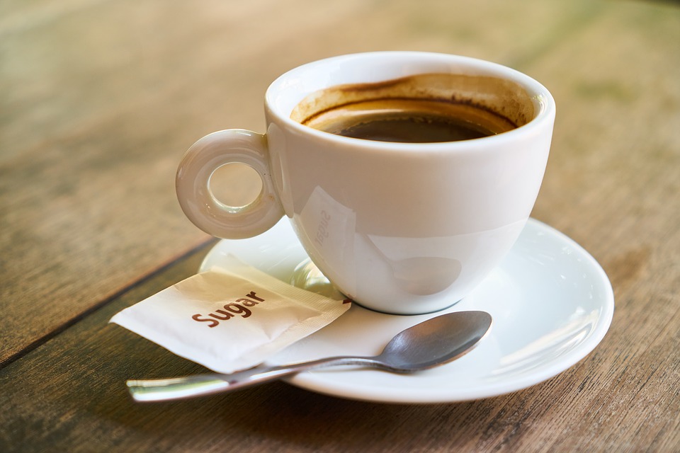 A white cup of black coffee on a saucer with a spoon and a packet of sugar.