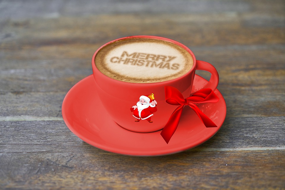 Red coffee cup with Merry Christmas foam art, a Father Christmas graphic, and a red bow.