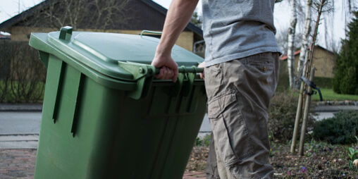 A person pulling a green plastic wheelie bin.