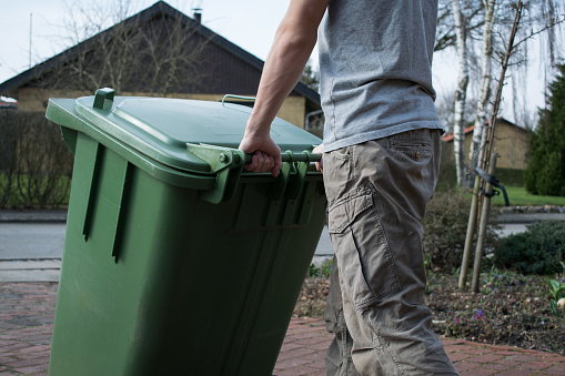 A person pulling a green plastic wheelie bin.
