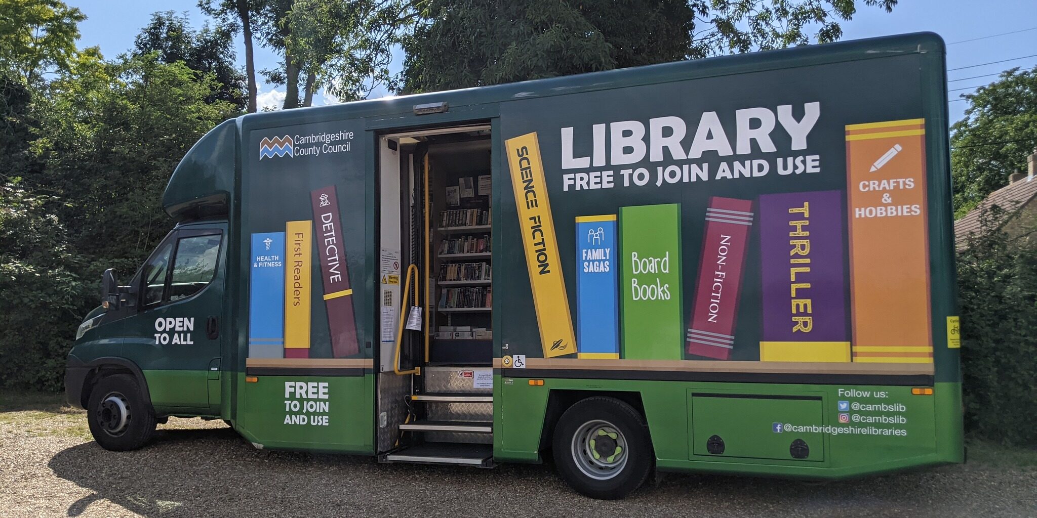 Green mobile library van with books painted on the side, parked outdoors with door open.