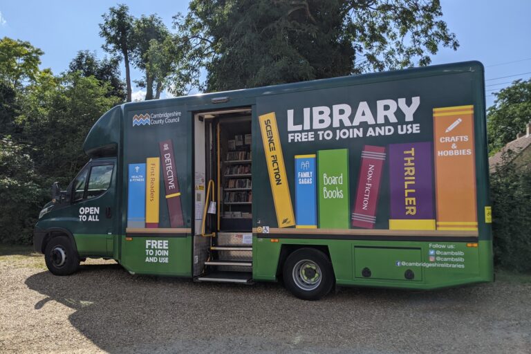Green mobile library van with books painted on the side, parked outdoors with door open.